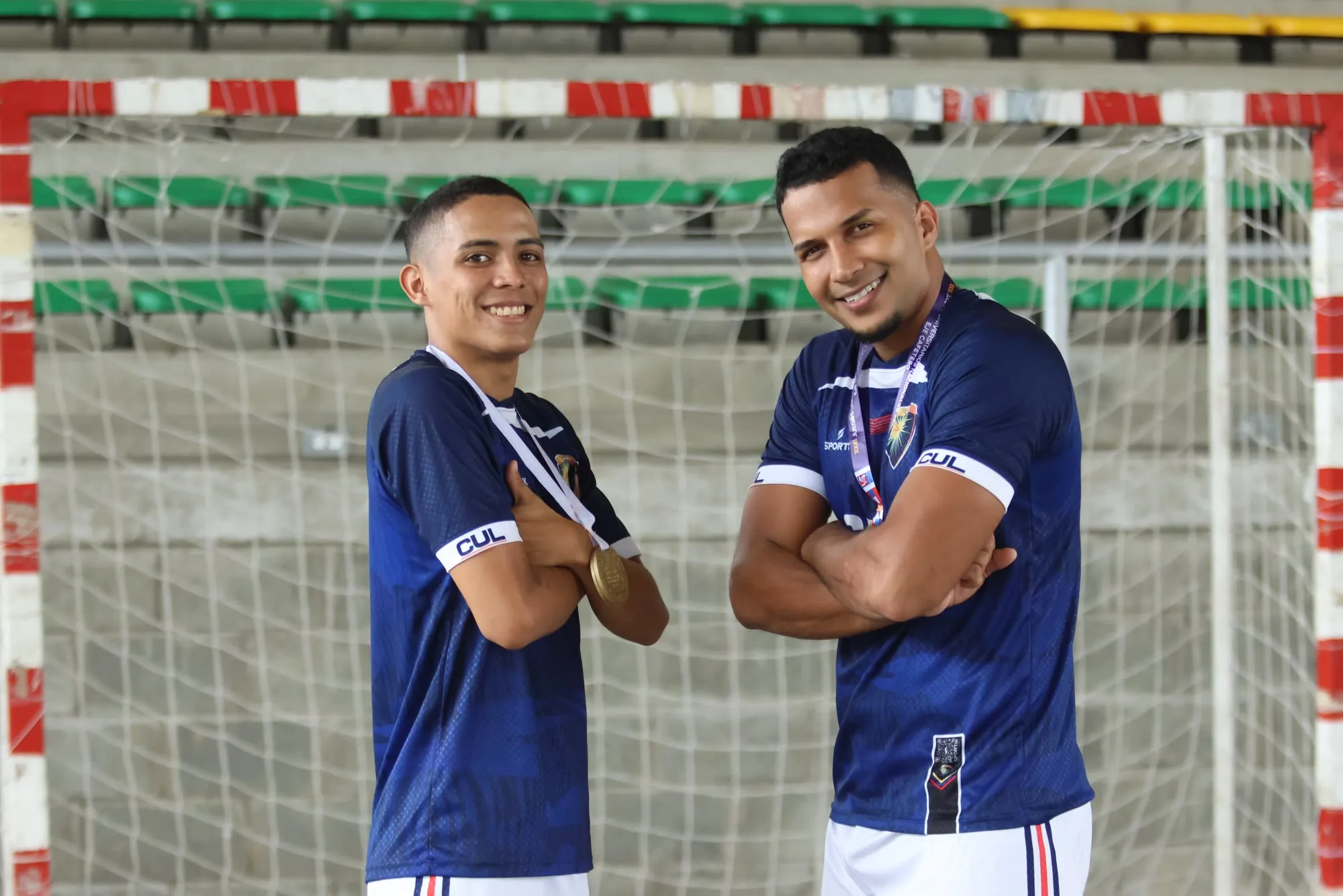 Dos jugadores de fútbol sala mostrando la medalla de oro frente al arco