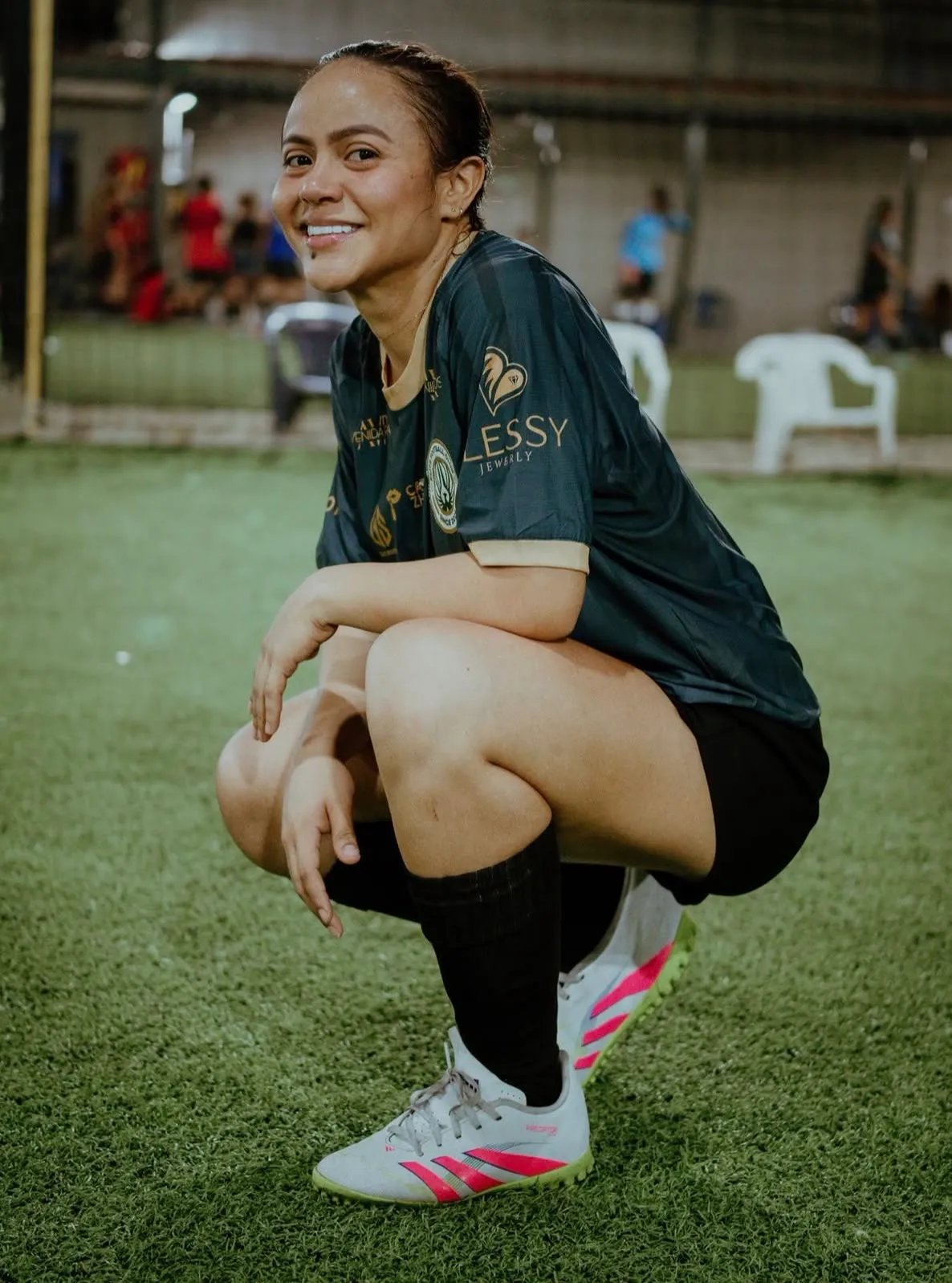 Jugadora en cuclillas sobre la grama sintética, sonriendo tras el entrenamiento nocturno